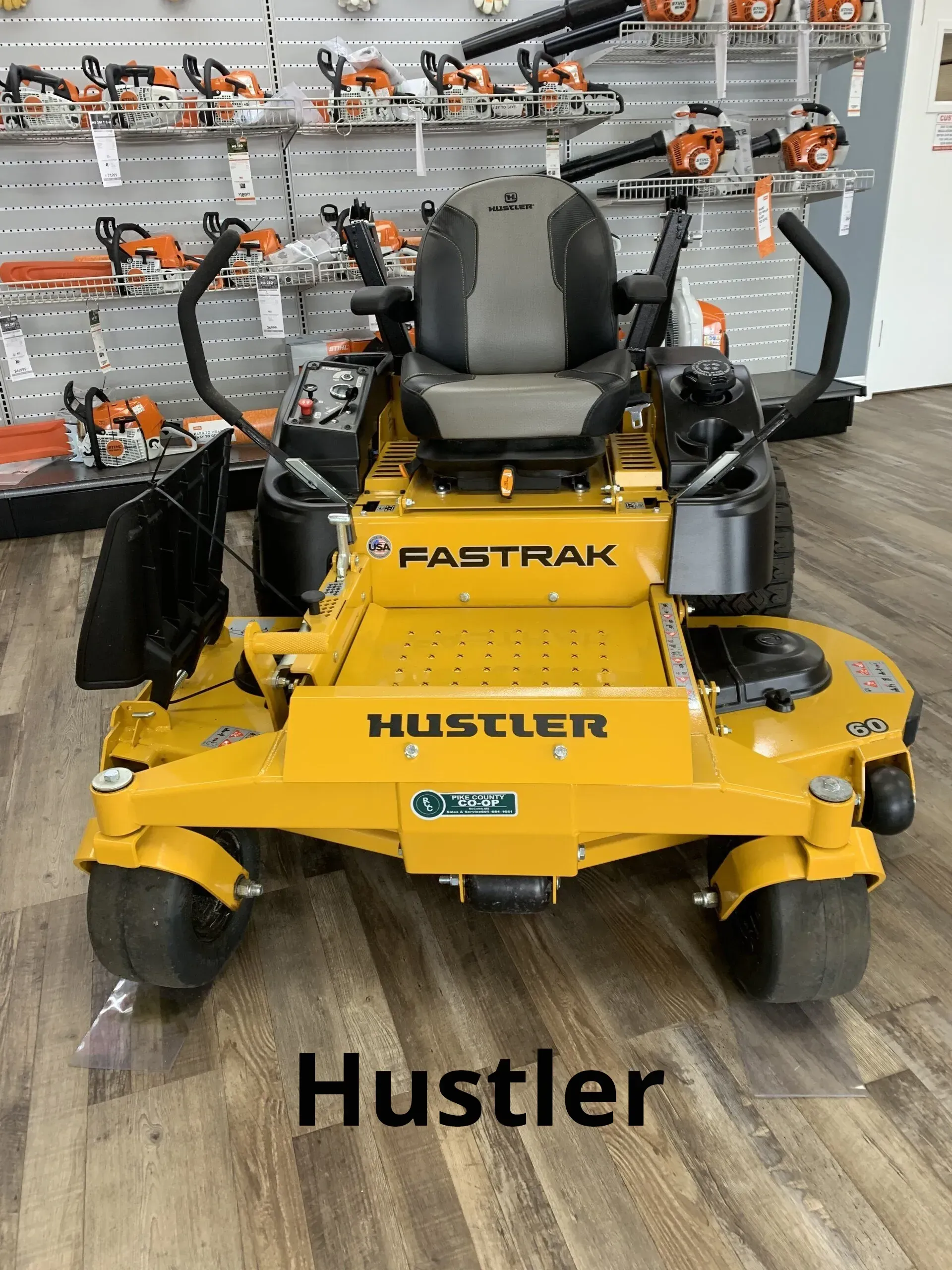 A yellow lawn mower is sitting on a wooden floor in a store.