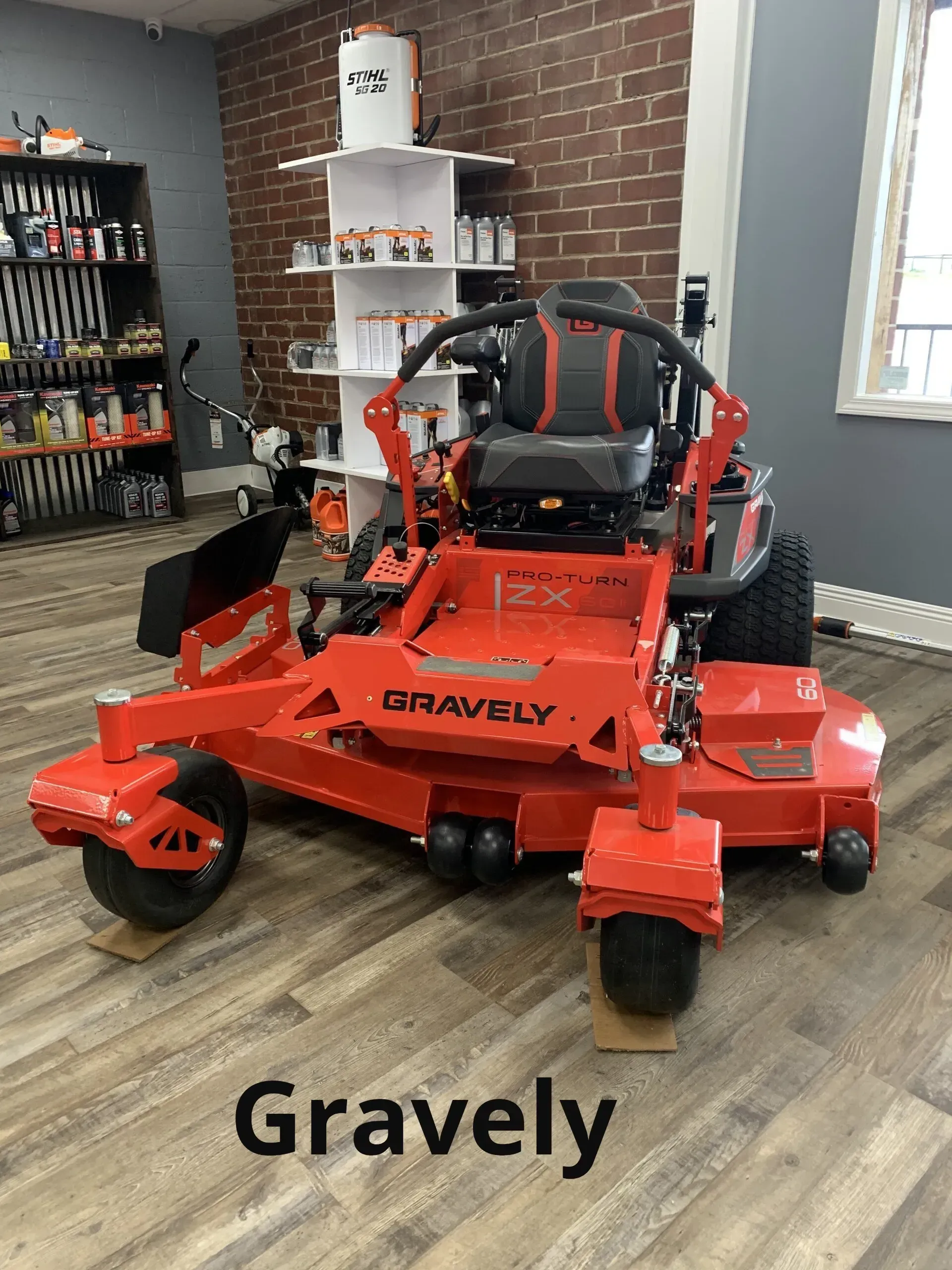 A gravely lawn mower is sitting on a wooden floor in a room.