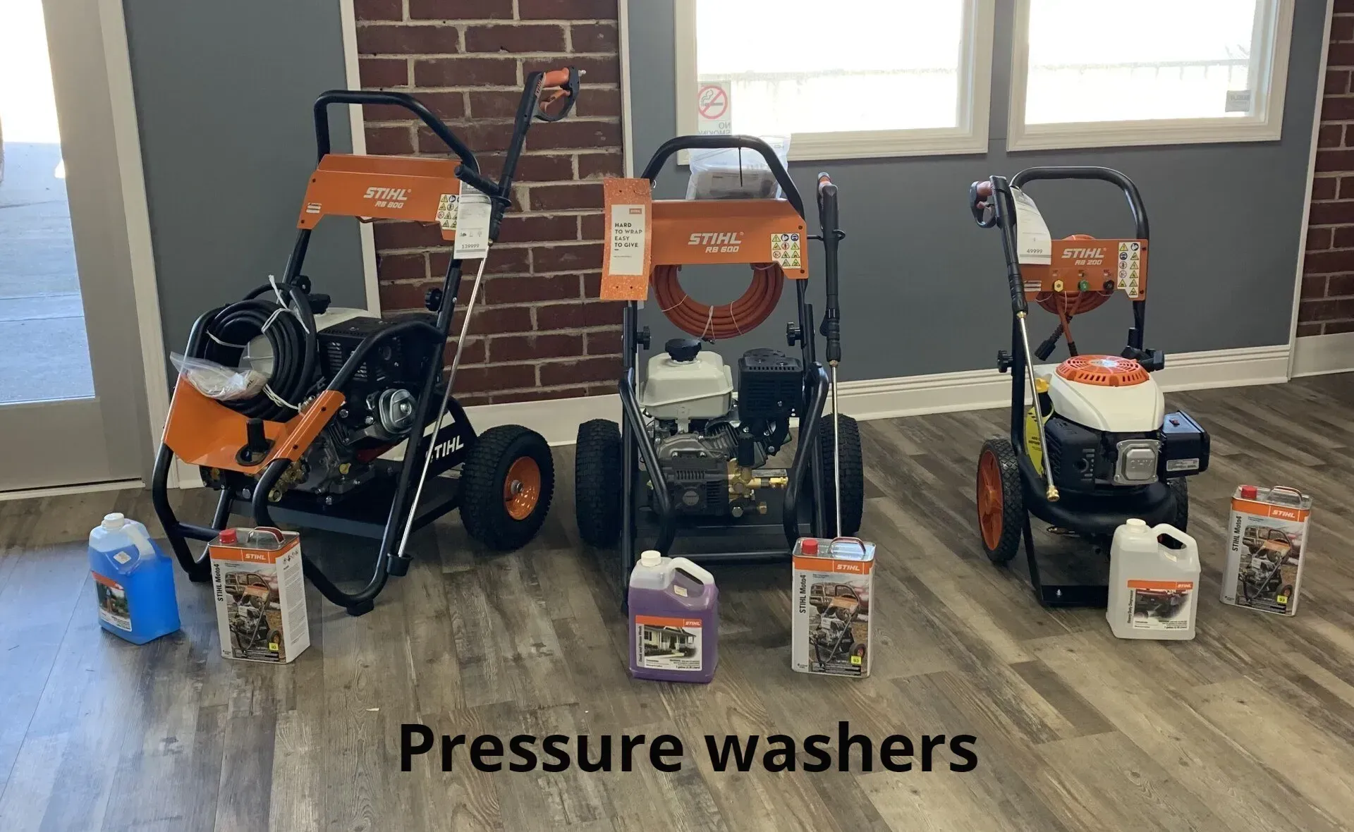 Three pressure washers are sitting on a wooden floor in a room.