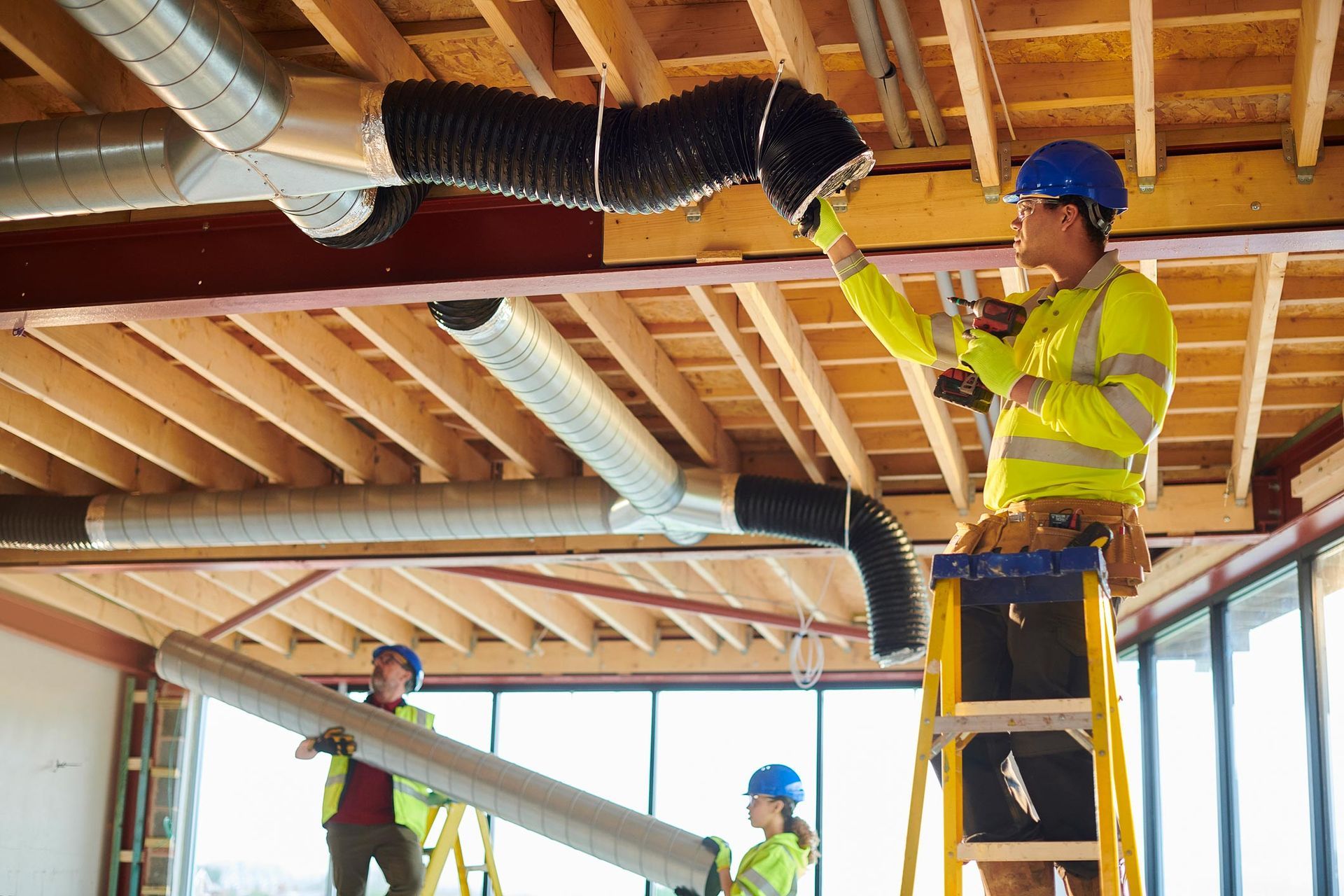Construction workers installing ventilation ducts in a building under construction, using ladders.
