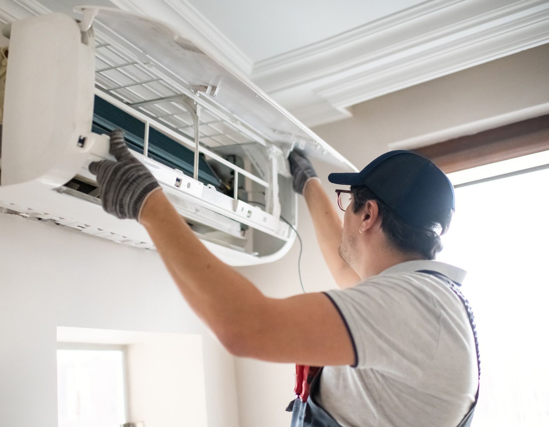 HVAC technician in gloves repairing a white wall-mounted air conditioner.