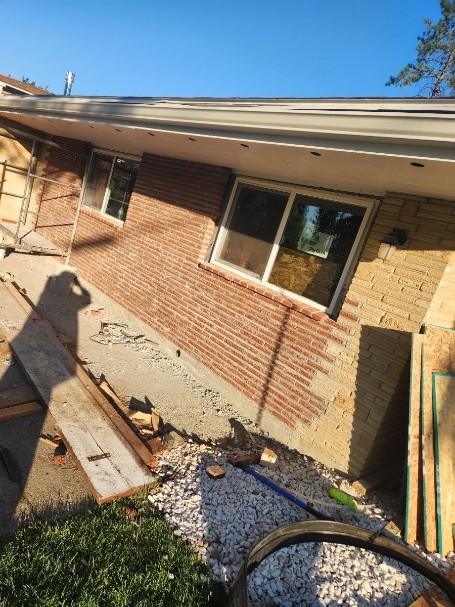 Brick and stucco home exterior under construction; boards, tools, and materials on the ground.