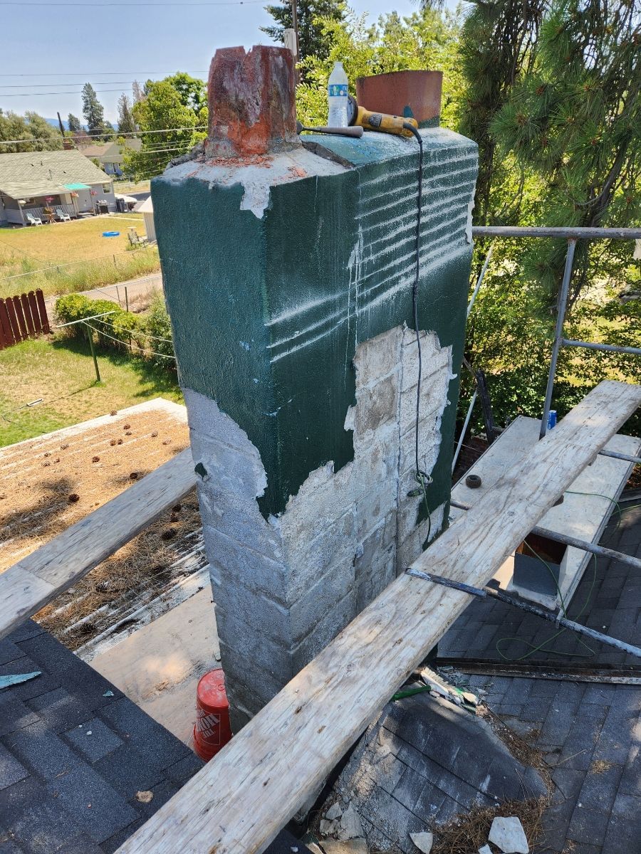 Chimney under repair on a roof; green coating partially removed, exposing brick.