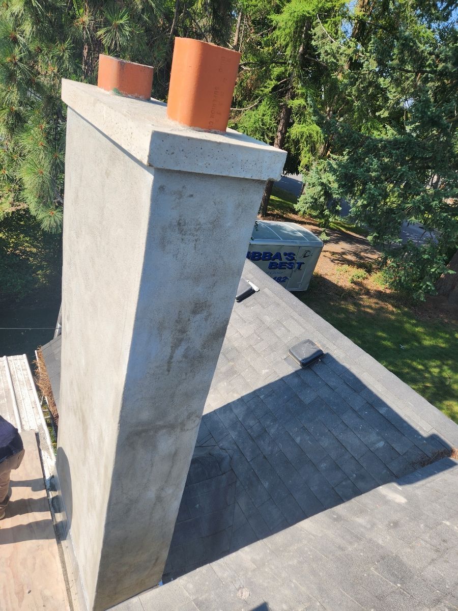 Concrete chimney on a sloped roof with two terracotta chimney pots. Green trees in background.