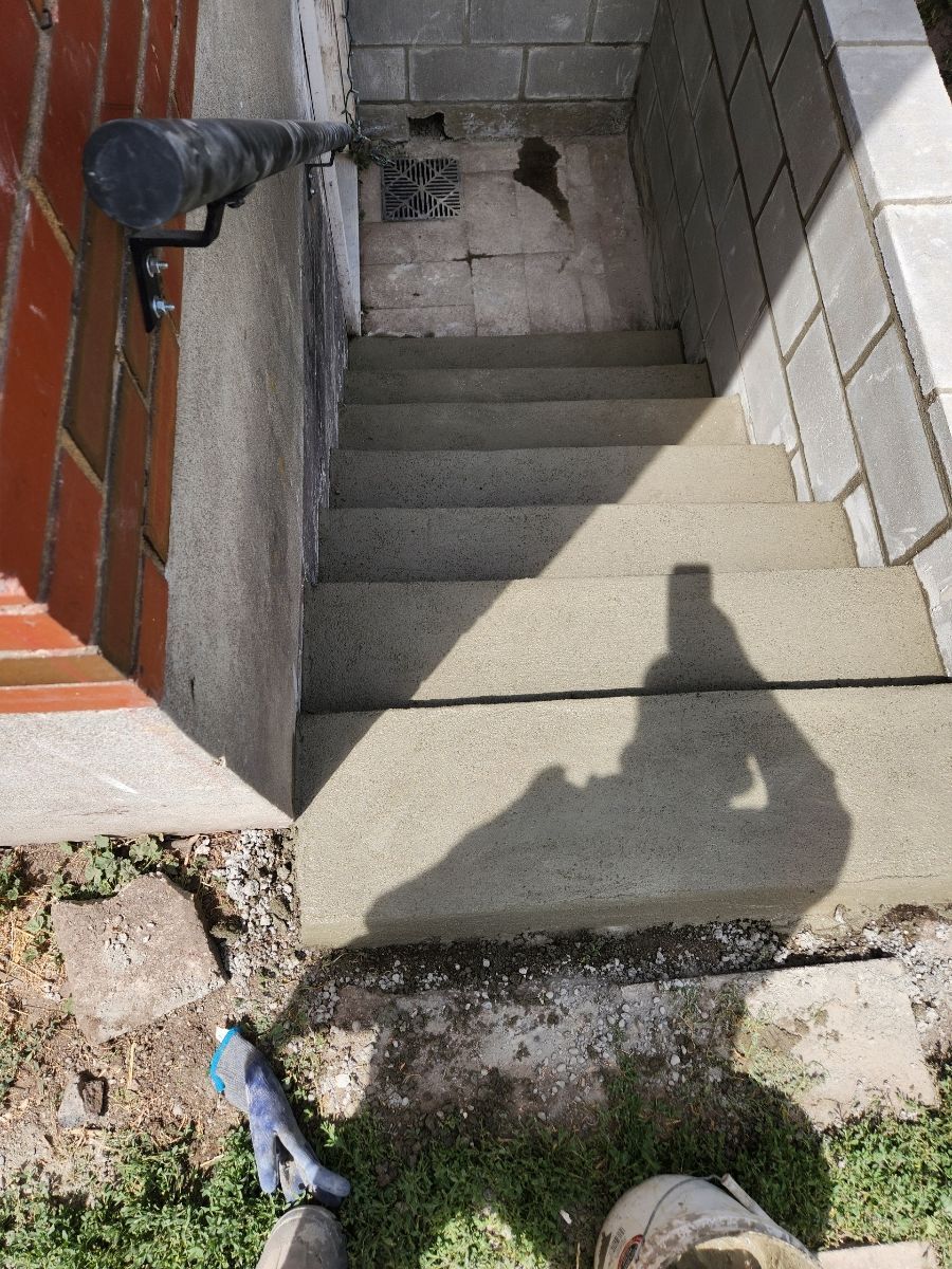 Concrete steps leading down to a basement entrance. Black pipe and a shadow of a person.