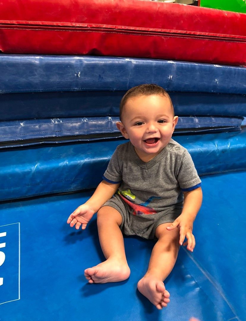 Smiling toddler sits on blue mat near stacked mats.