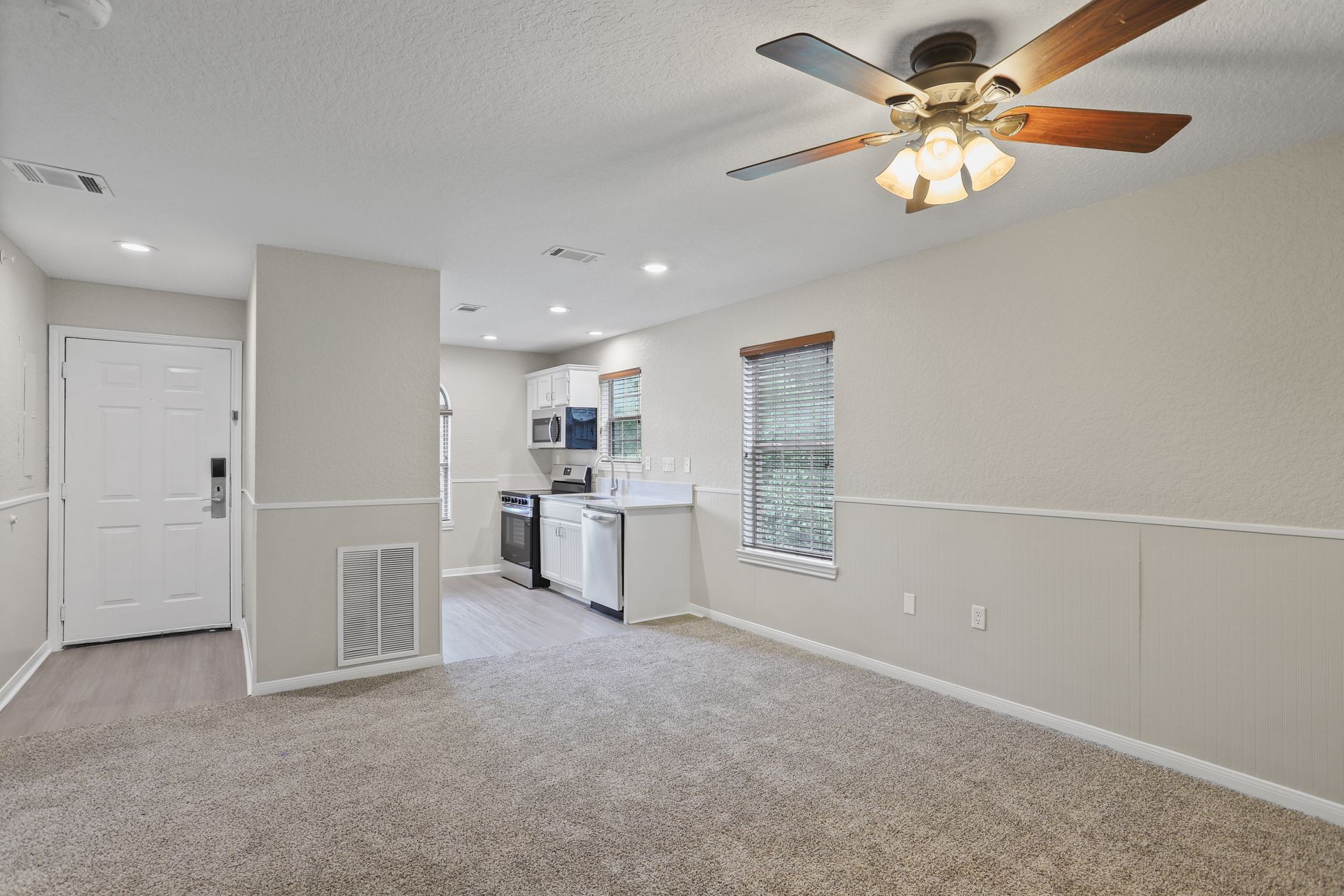 Photo of a living room with a ceiling fan and a kitchen in the background