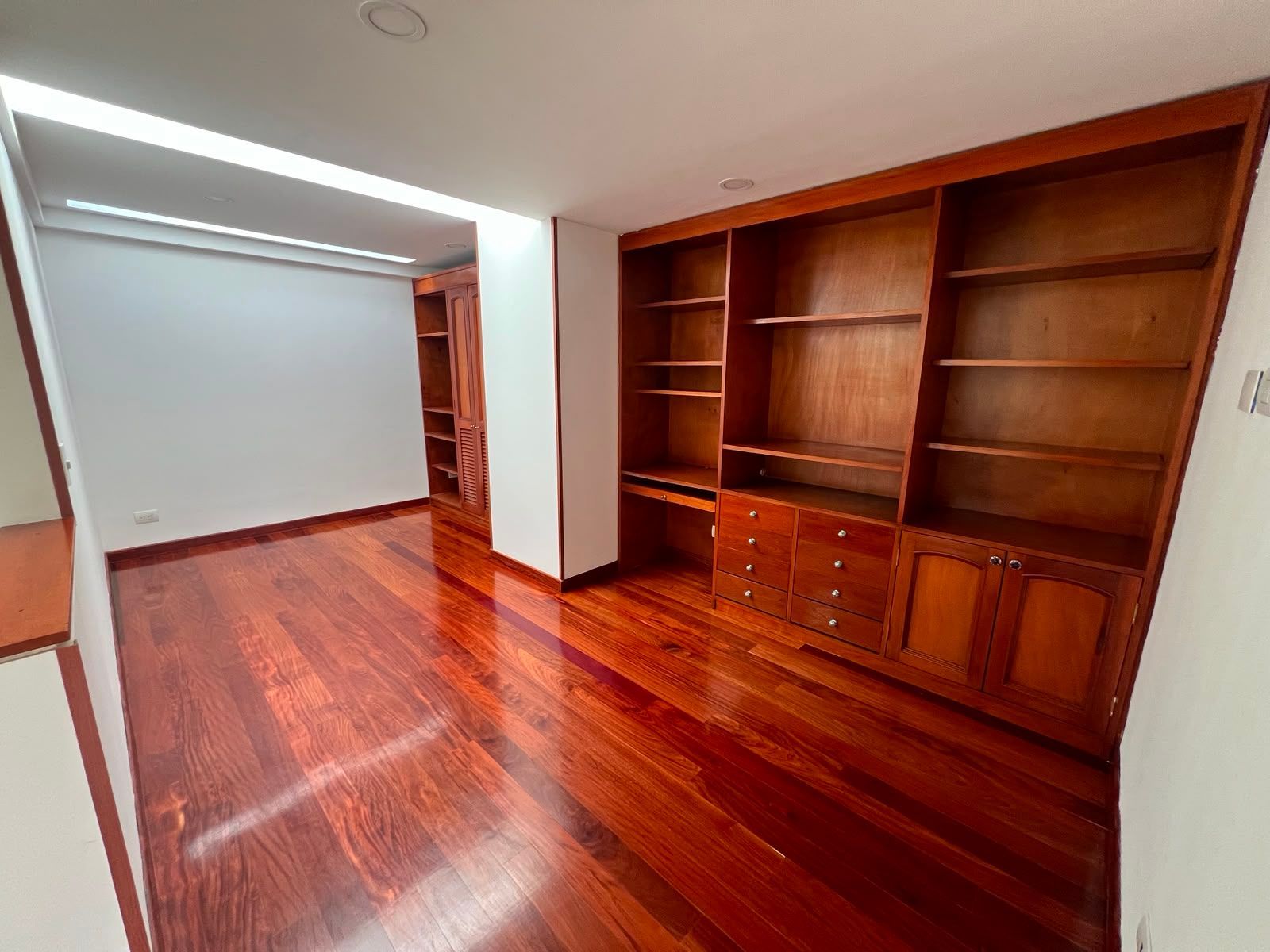 Habitación vacía con suelo de madera pulida, estanterías de madera empotradas y paredes blancas.