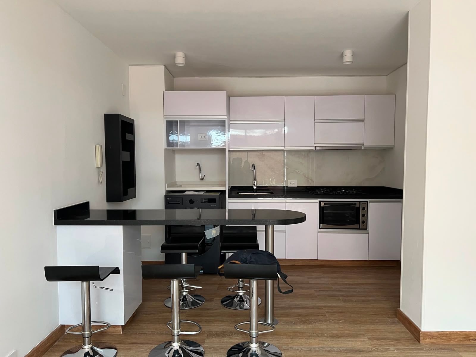 Cocina moderna blanca con encimeras negras, taburetes de bar y suelo de madera.