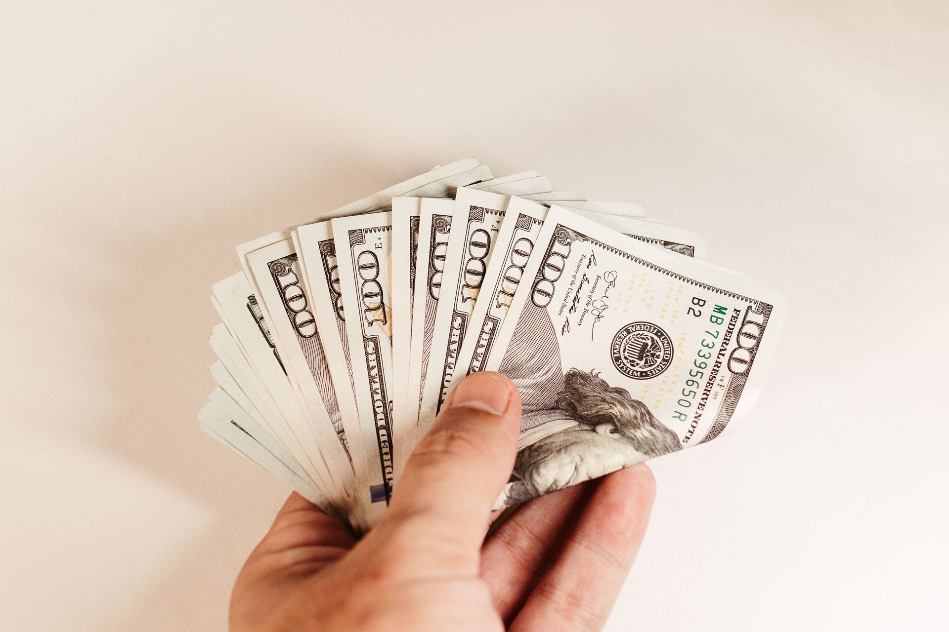 Hand holding a fan of U.S. dollar bills against a plain light background