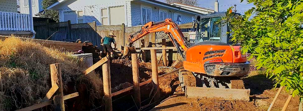 An excavator is digging a trench in front of a house.