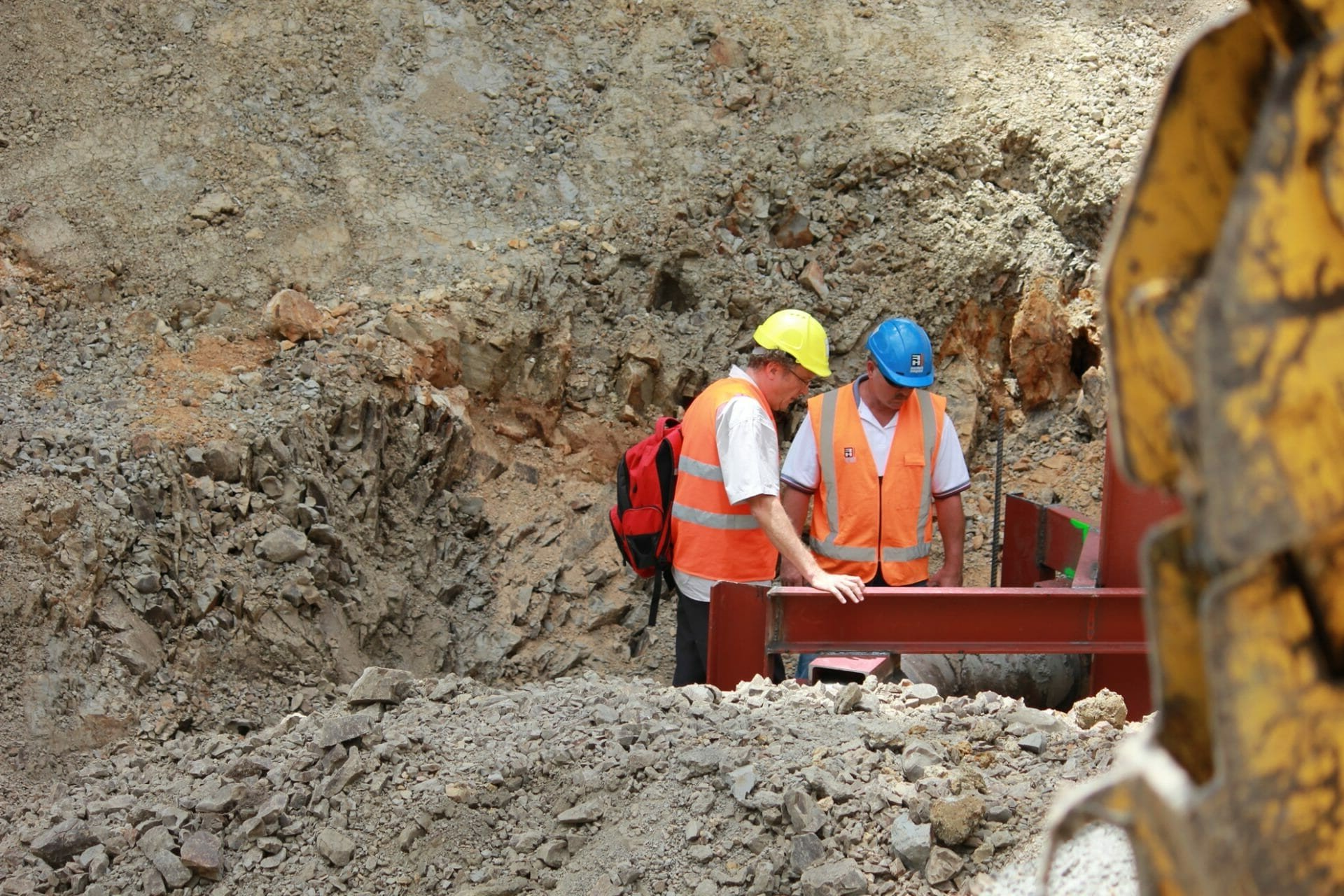 Two construction workers are standing in the dirt looking at a piece of metal.