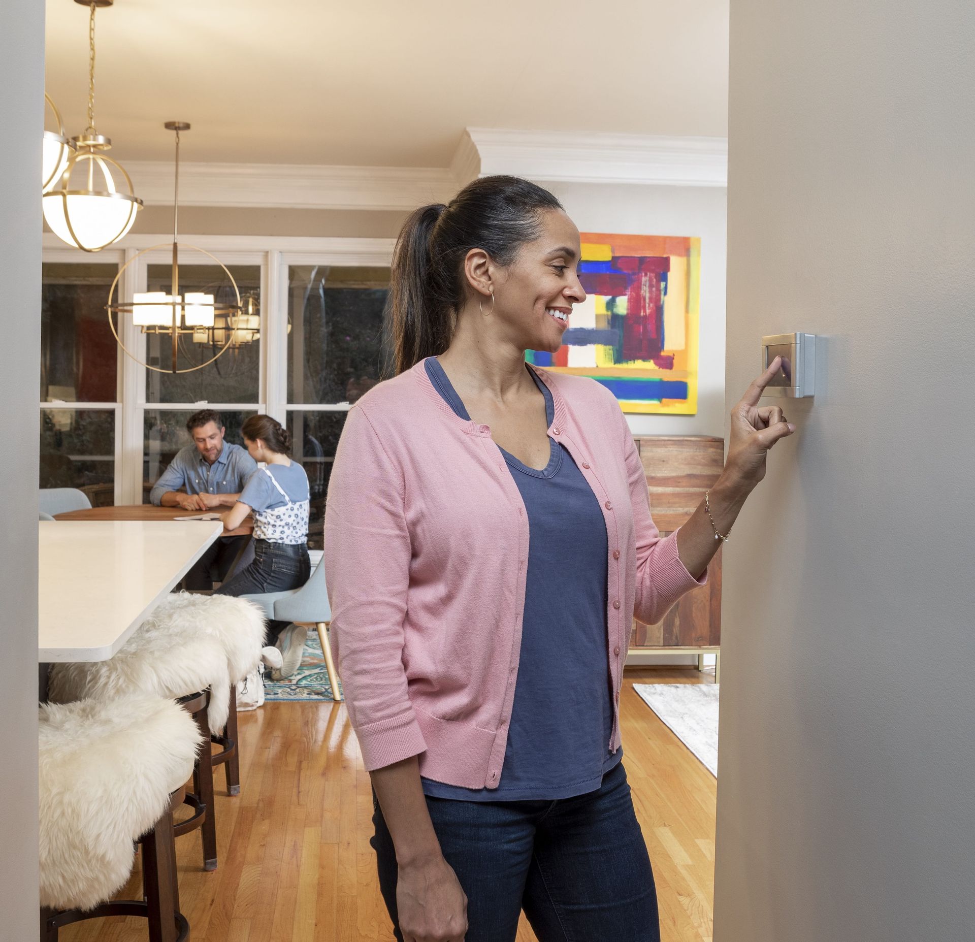 A woman in a pink cardigan is adjusting a thermostat in a living room.