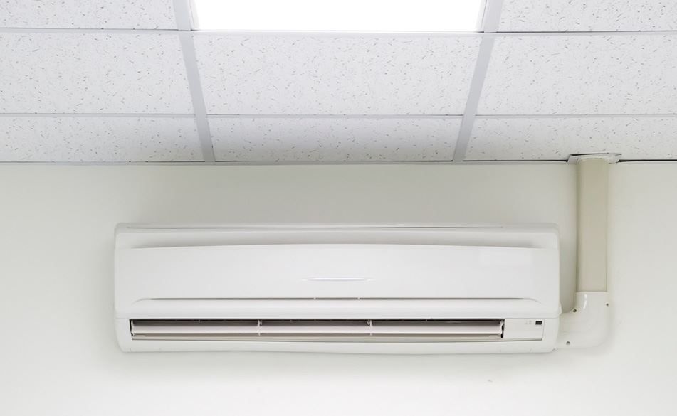 A white air conditioner is hanging on a white wall next to a ceiling.