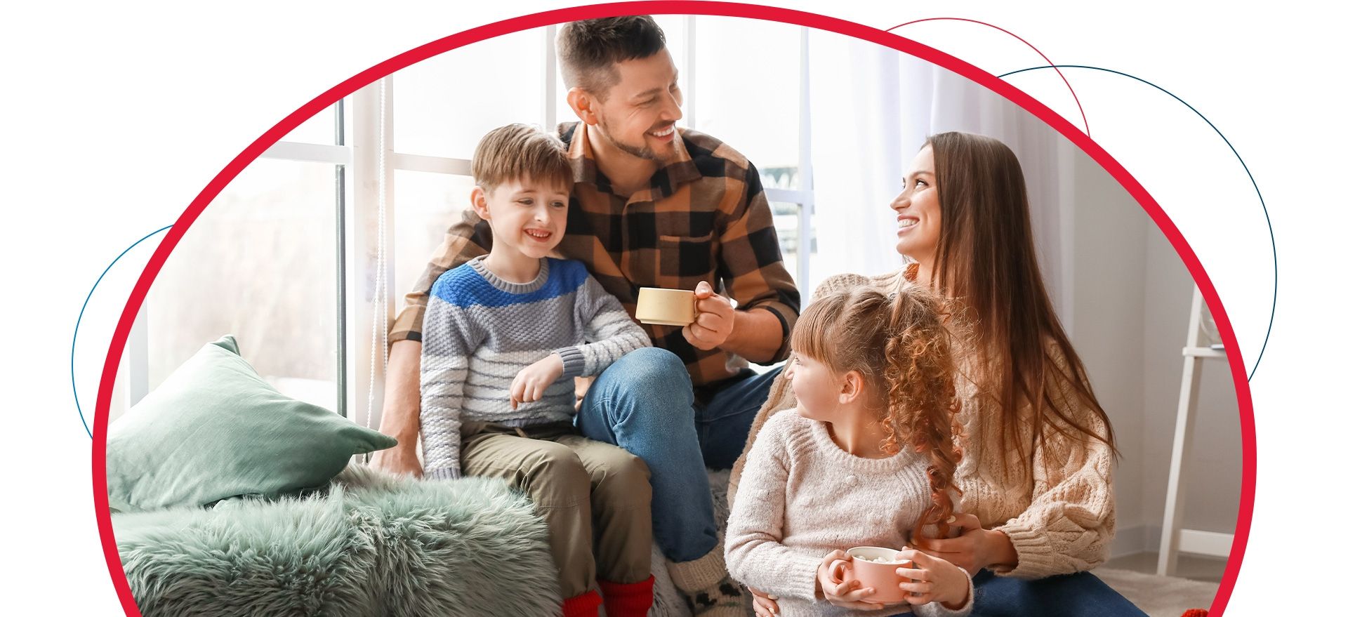 A family is sitting on the floor in front of a window drinking coffee.