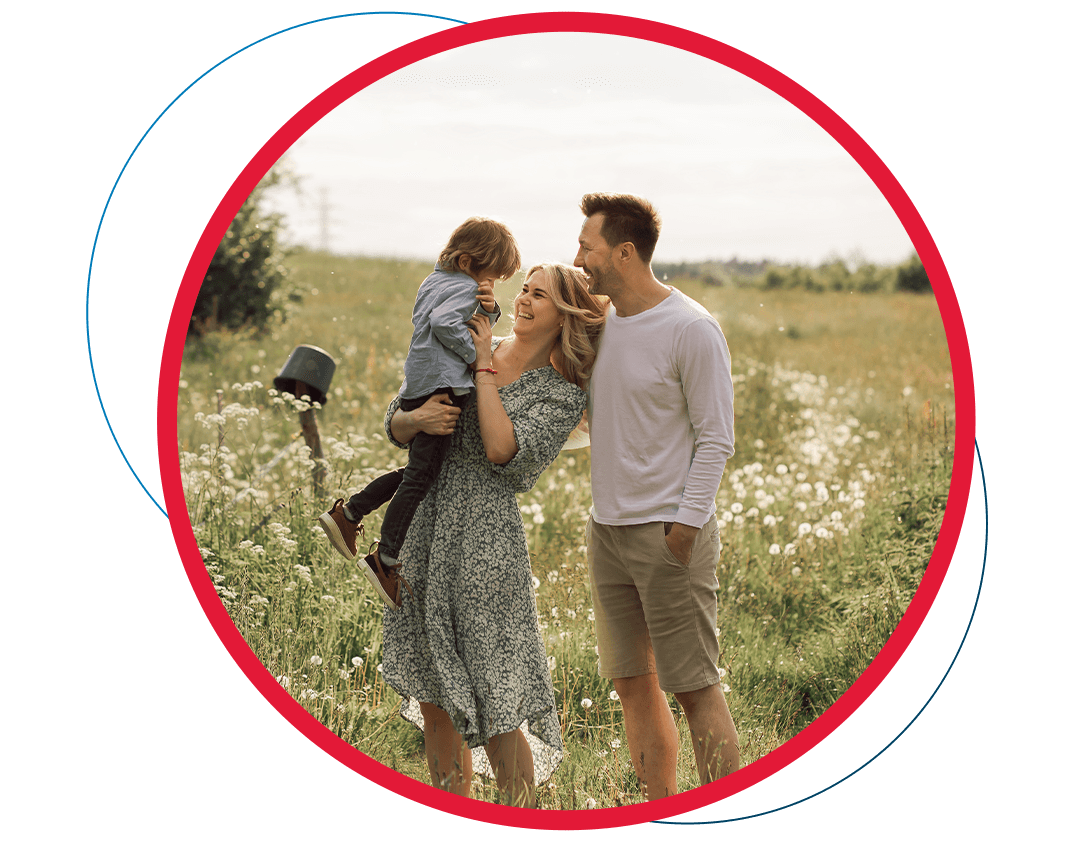 A family is standing in a field holding a child.
