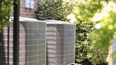 Two air conditioners are sitting outside of a brick building.