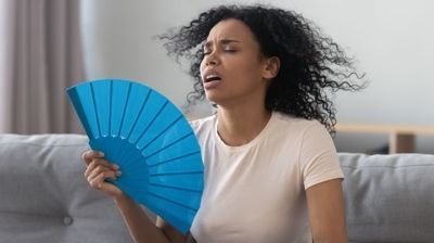 A woman is sitting on a couch holding a blue fan.