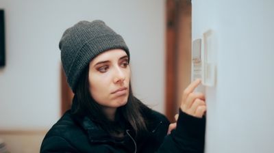A woman in a hat is adjusting a thermostat on a wall.