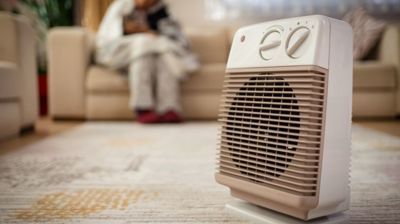 A person is sitting on a couch in front of a heater in a living room.