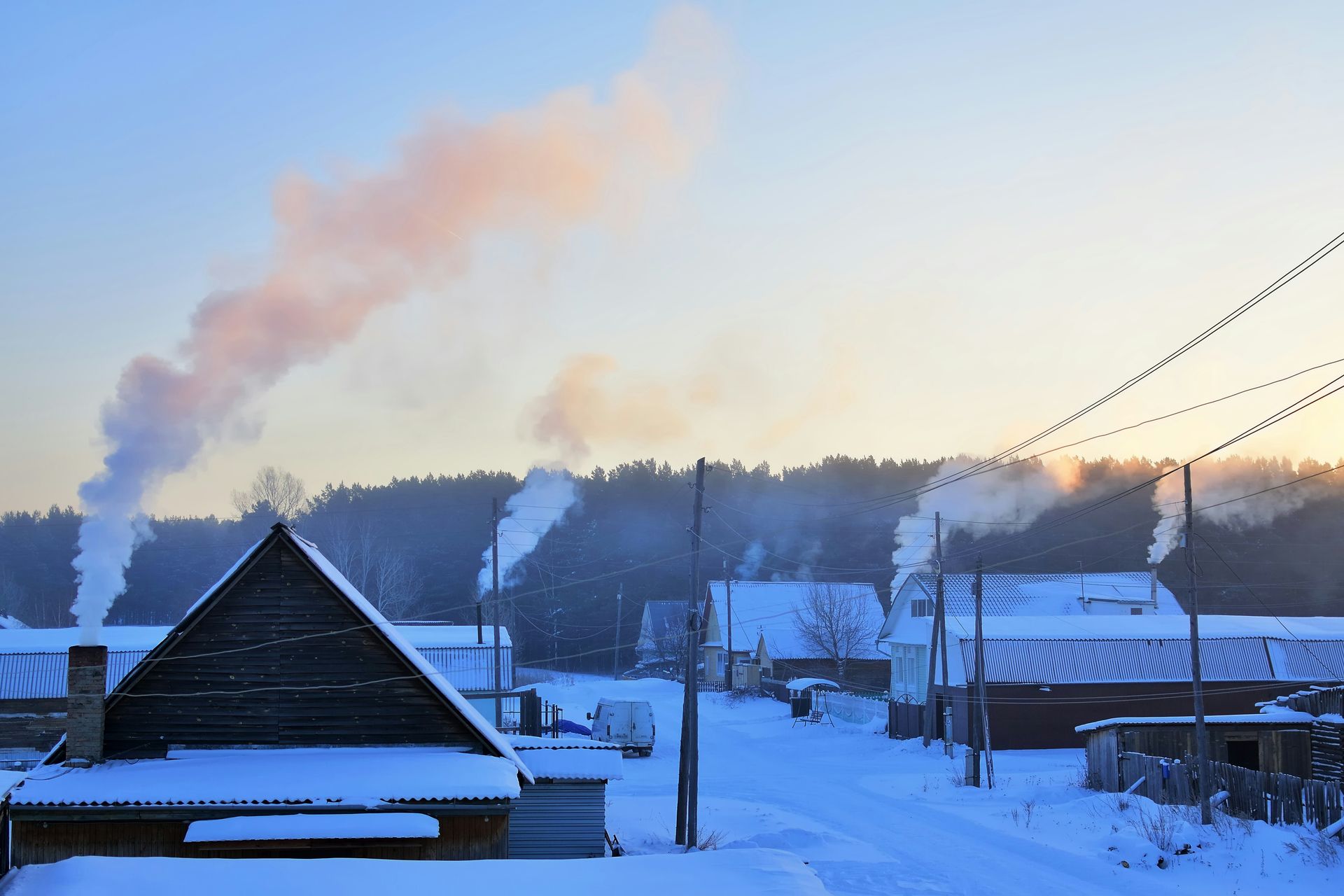 Snowy village scene with smoke rising from chimneys into a pale blue sky.