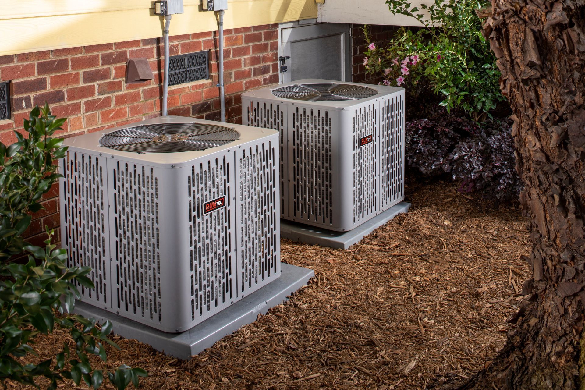 Two air conditioners are sitting outside of a house.