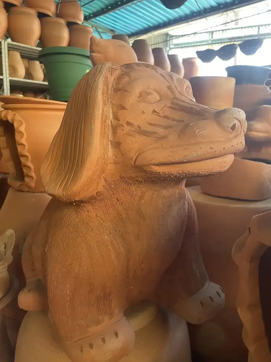 Una estatua de arcilla de un perro está sentada encima de una pila de ollas.
