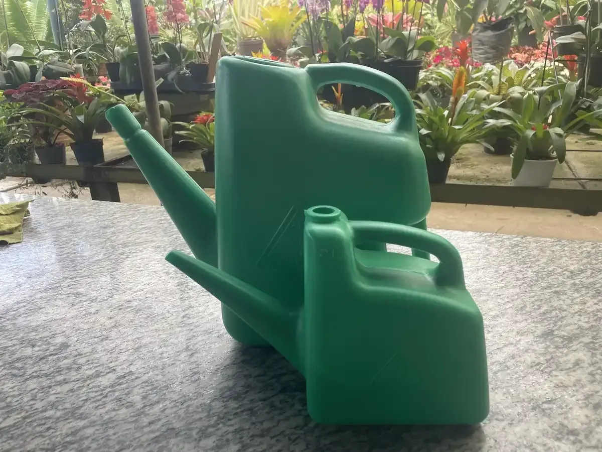 Dos regaderas verdes están sobre una mesa con flores en el fondo.