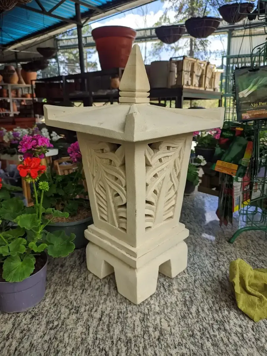 Una lámprara blanca está colocada sobre una alfombra al lado de flores  y plantas.