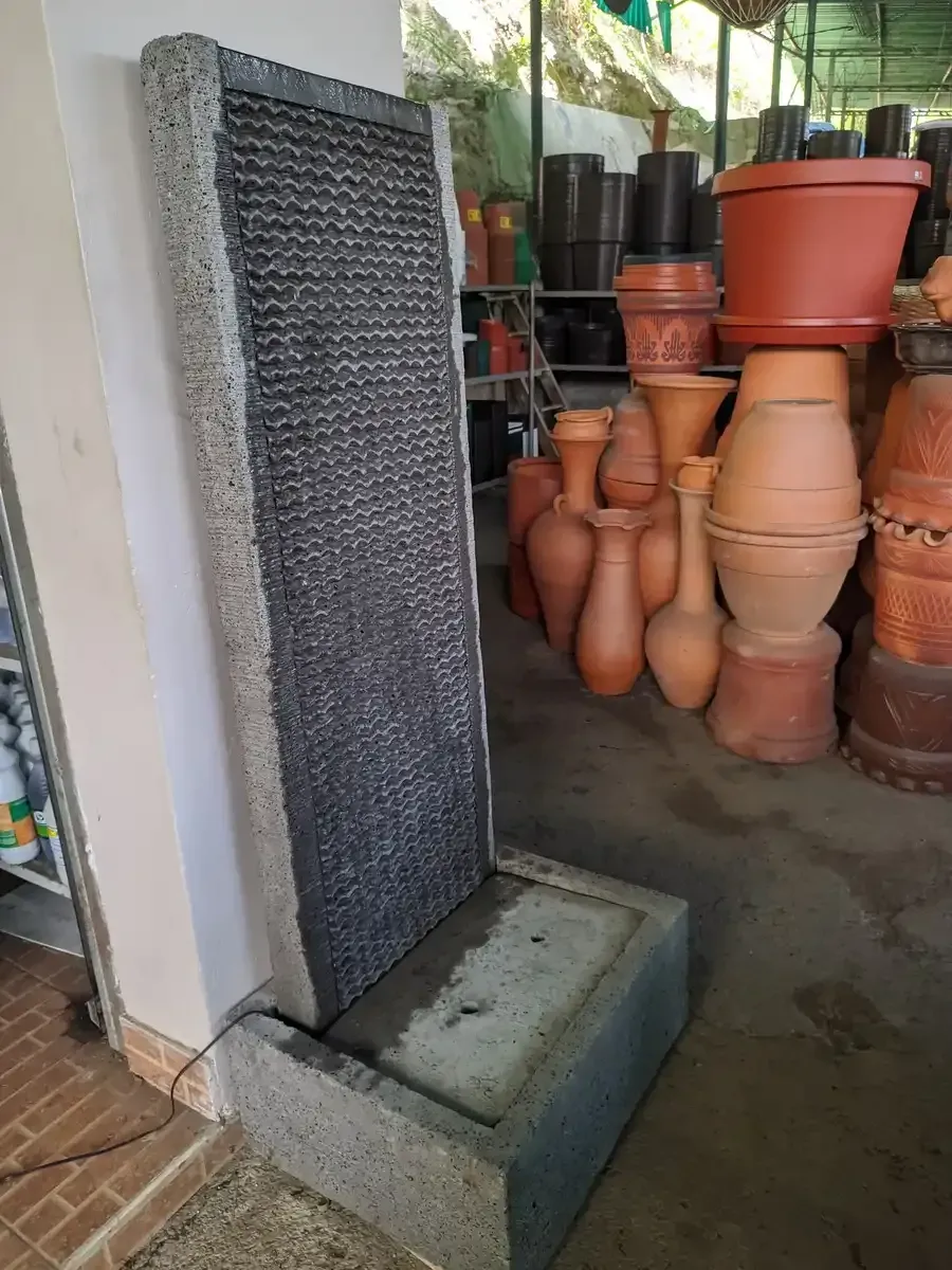 Una fuente en piedra de agua está al lado de una pila de macetas en una tienda.