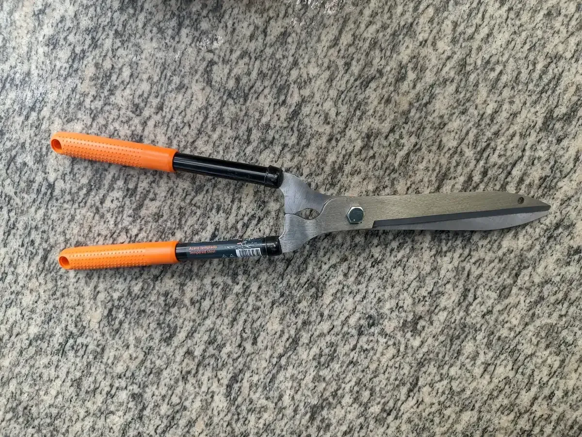 Un par de tijeras de podar con mangos de color naranja se encuentran sobre una alfombra.