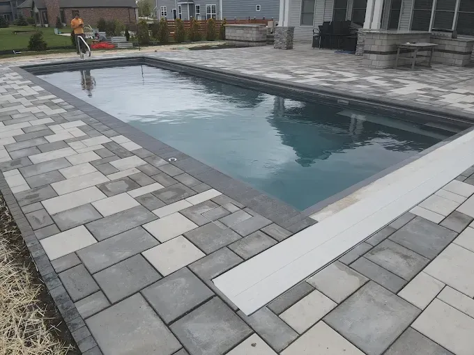Rectangular pool with gray paving, light-colored coping, and a diving board. A person is in the background.
