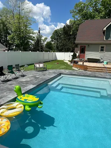 Backyard pool with blue water, a turtle floatie, and a house in the background under a blue sky.