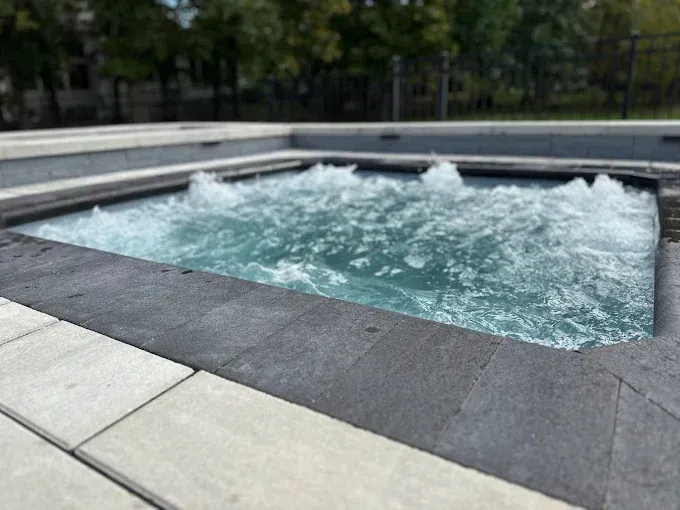Bubbling hot tub with dark grey border, set in light grey tiled area, outdoor setting.