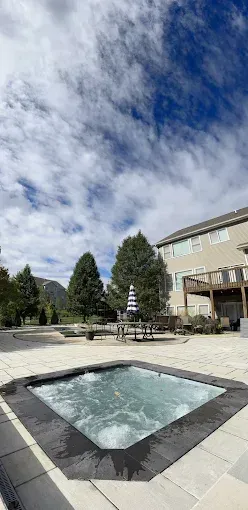 A hot tub in a backyard with trees, mountains, and a cloudy blue sky.