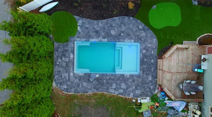 Overhead view of a turquoise rectangular pool with dark gray patio, surrounded by green lawn and landscaping.
