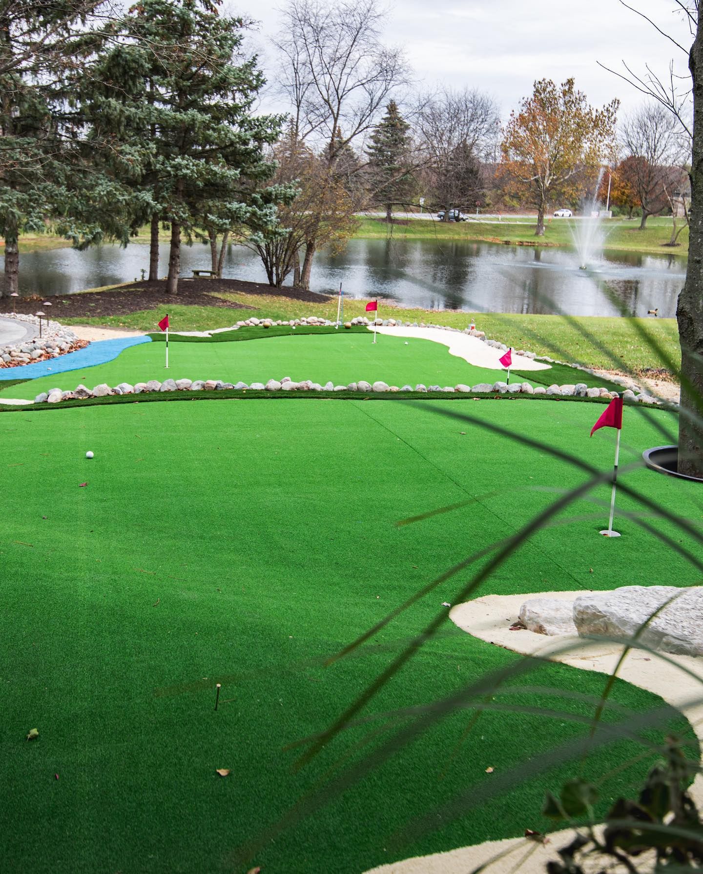 Miniature golf course with green turf, water feature, and red flags.