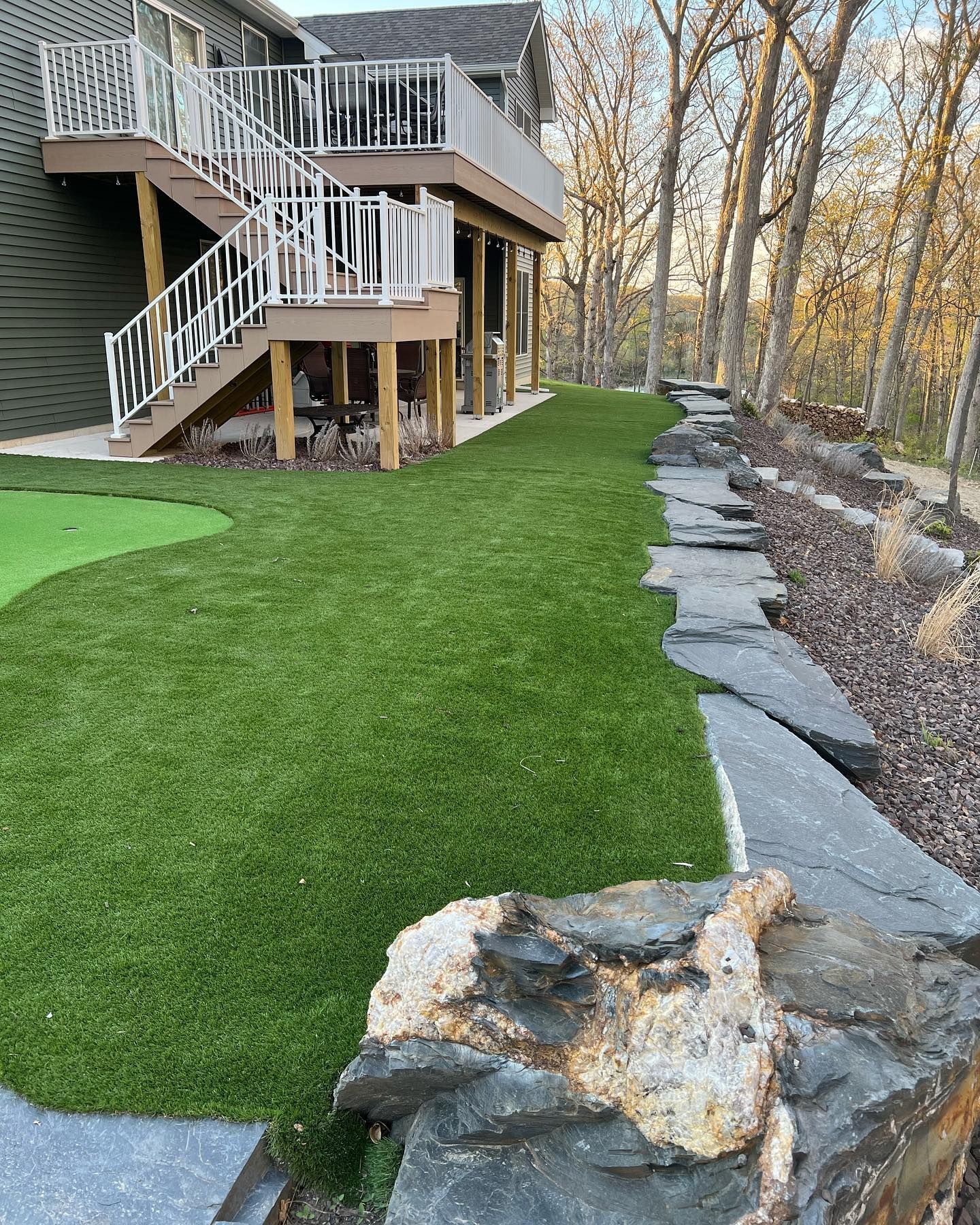 Green lawn next to a house with a deck and stone retaining wall.