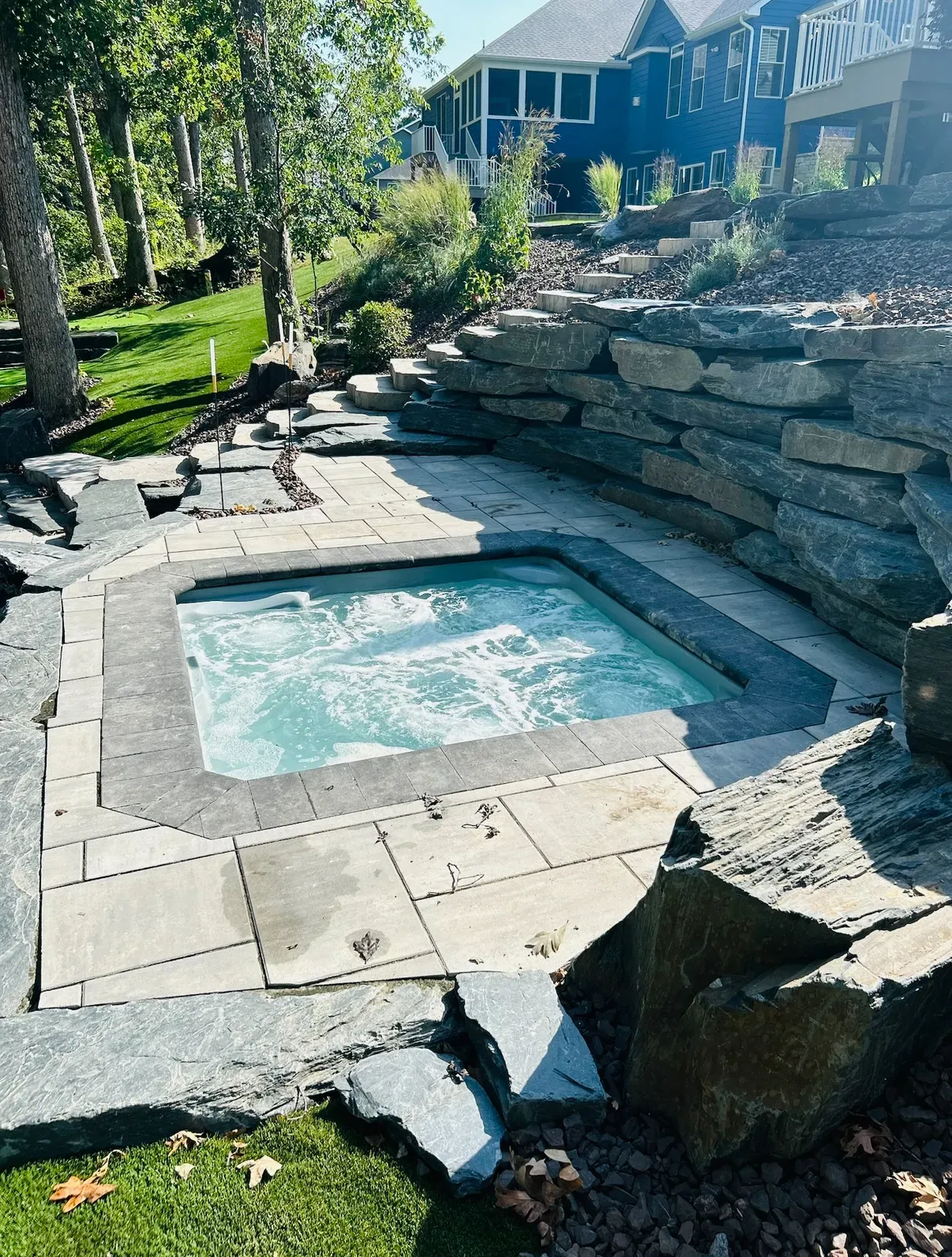 A hot tub set into stone, surrounded by landscaping and a retaining wall.