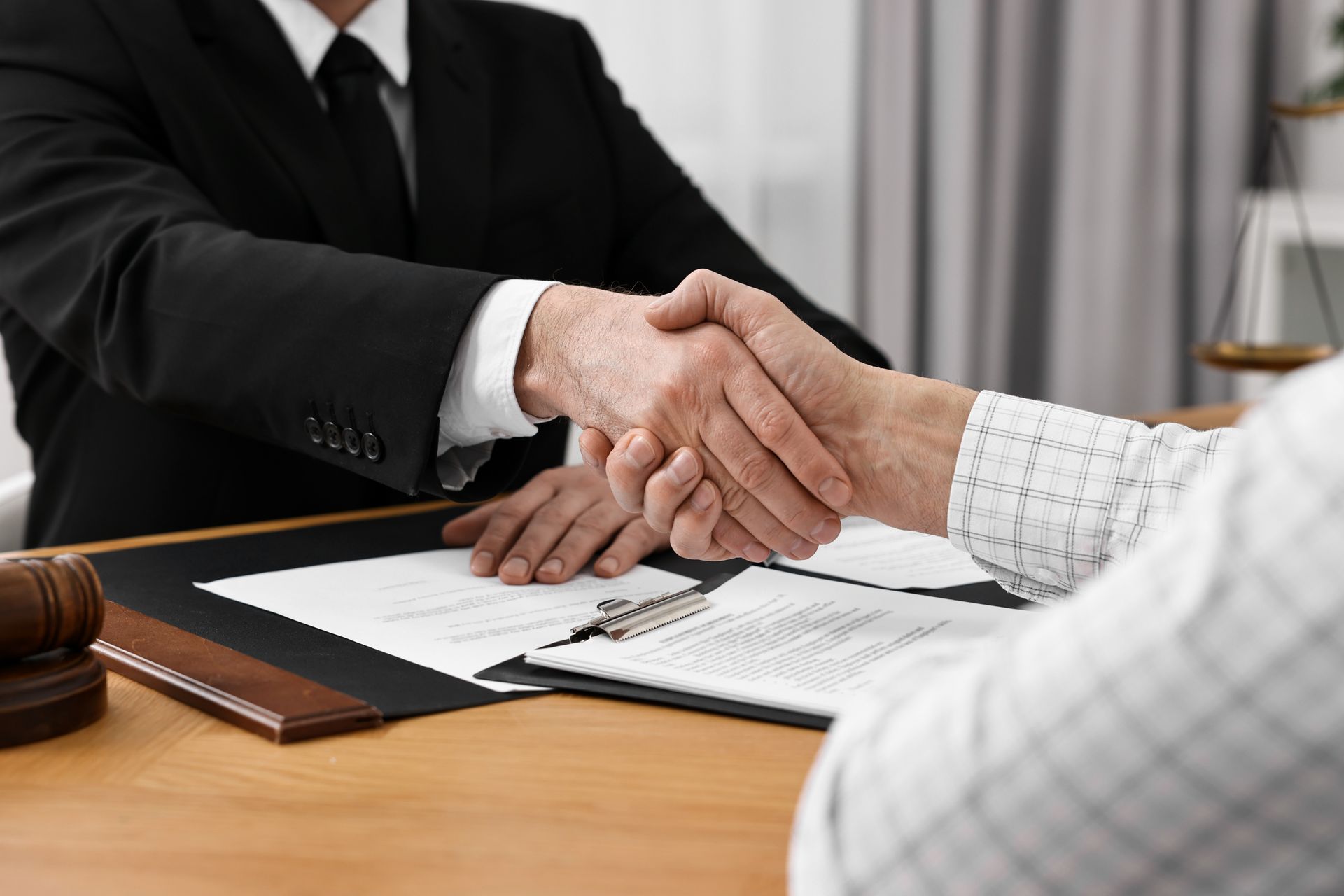 Lawyer and client shaking hands over legal documents on a desk.