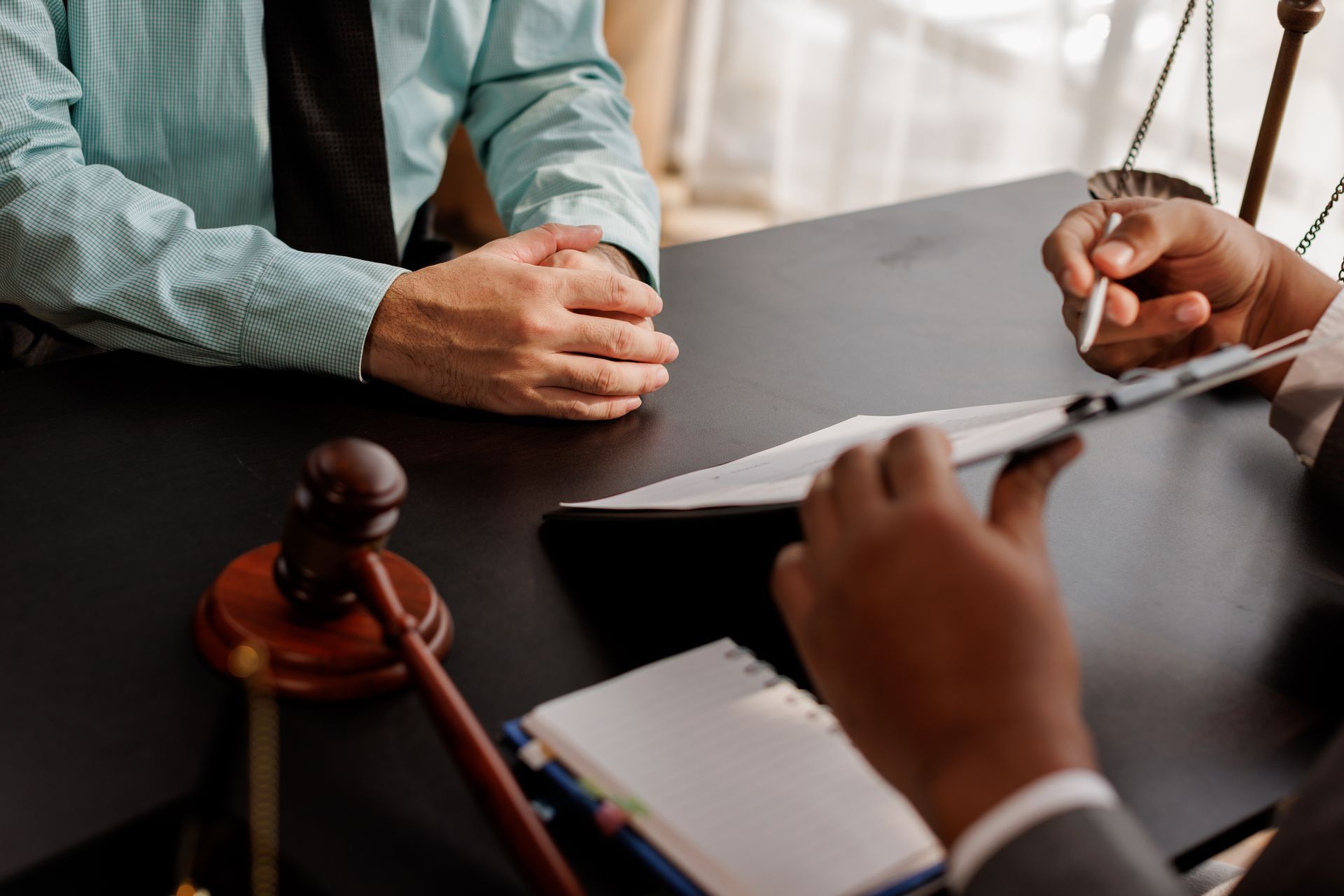 Two people review legal documents with gavel and justice scales visible on the table Two people review legal documents with gavel and justice scales visible on the table