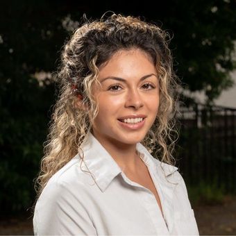 A woman with curly hair is wearing a white shirt and smiling for the camera.
