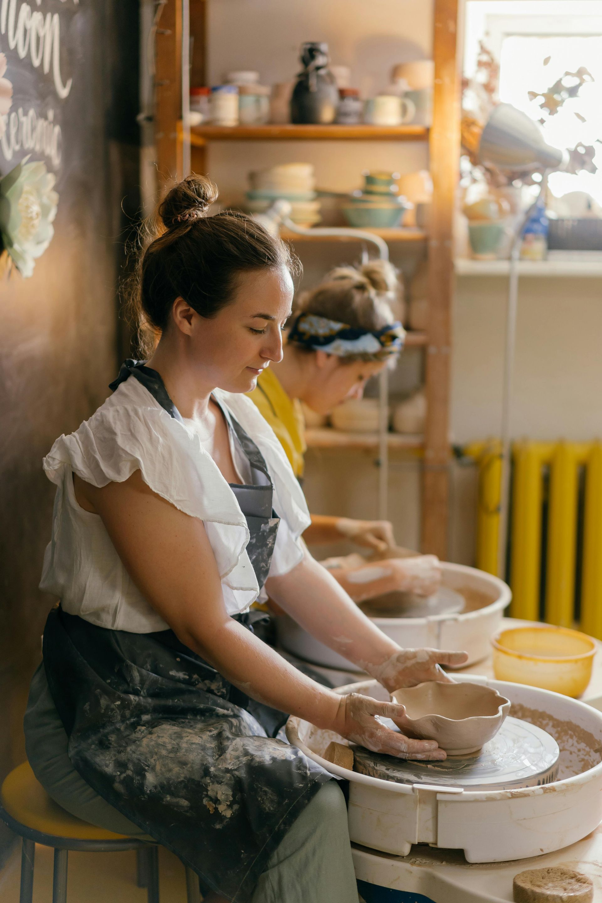 A woman is sitting on a pottery wheel making a bowl.