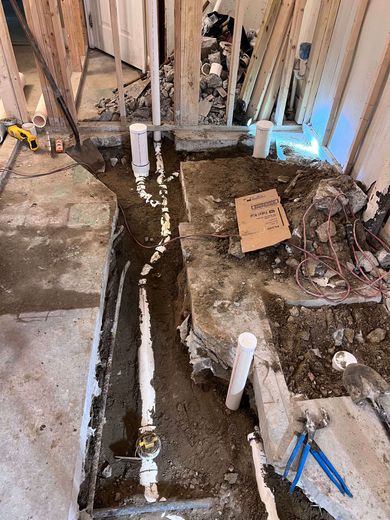 Bathroom renovation in progress with exposed plumbing pipes in a trench.