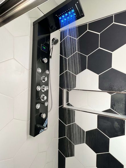 Black shower panel with blue overhead lights, next to hexagonal black and white tiled wall.