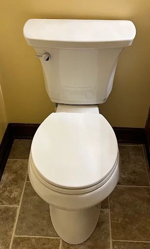 White toilet on tile floor in a bathroom. Tank has a chrome flush handle.