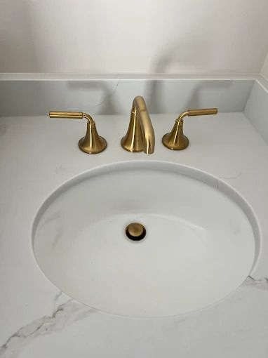 White bathroom sink with gold faucet and handles on white countertop.