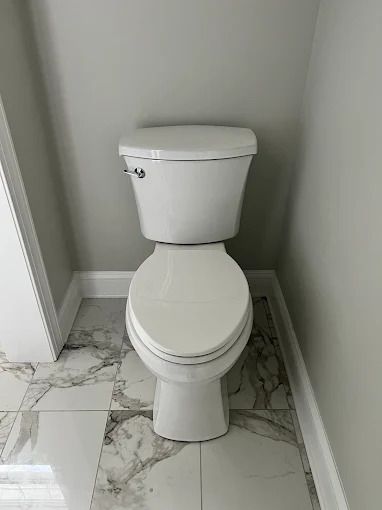 White toilet in a small bathroom with marble-look flooring and gray walls.