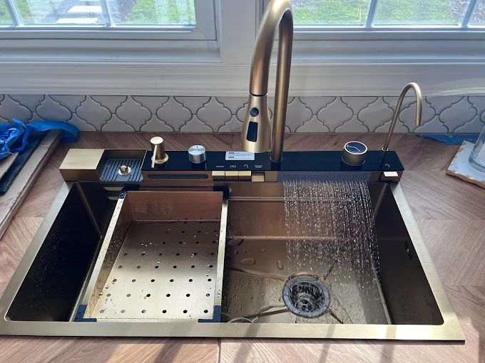 Gold kitchen sink with integrated faucet, accessories, and running water.