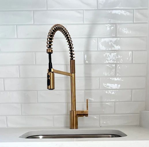 Gold kitchen faucet with black coil against white subway tile backsplash.